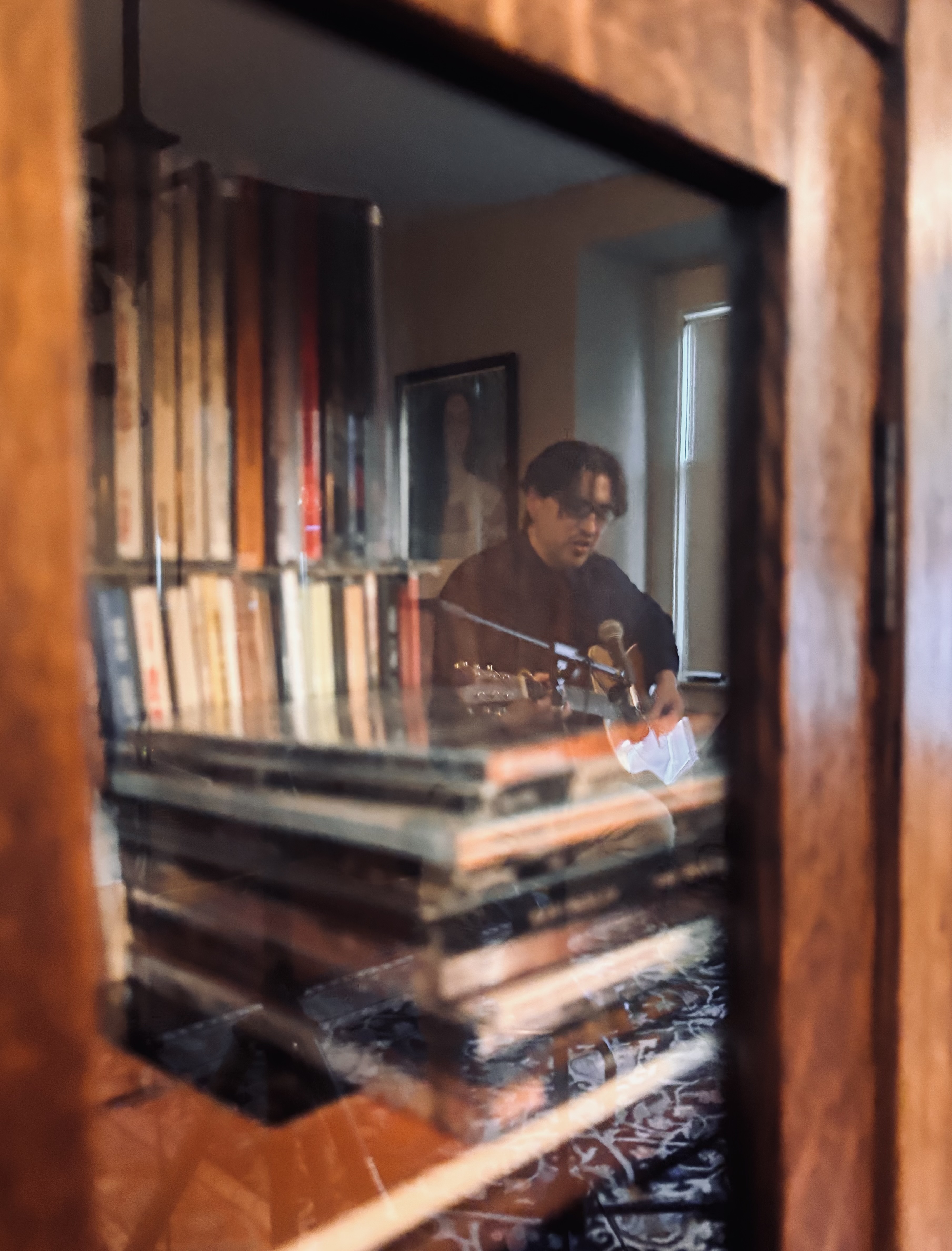 Performing at a house concert, reflected in a bookcase mirror